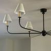 Close-up angled view of chandelier arms showing matte black finish and cream linen tapered shades