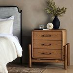 Nightstand styled in bedroom setting next to grey upholstered bed with decor on top
