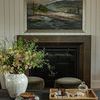 Painting above fireplace with decorative elements like flower vase and tray on a coffee table in front