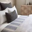 dark gray Murphy Pillow arranged on bed with white pillows and striped blue throw