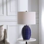 Luke Table Lamp shown on white round side table next to light-colored fabric sofa in a white paneled room