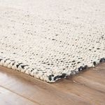 Close-up corner edge displaying braided white and black jute fibers against wood floor
