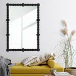 Mirror hung on white wall above mustard yellow sofa with pillows and natural decor accents