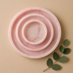 Three nested pink alabaster trays on beige background with green leafy branch beside