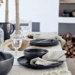 Smaller black bowl on a black plate with utensils and linen napkin, rustic dining table setting