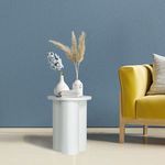 Styled room scene with bright yellow sofa, blue textured wall, and Solstice End Table holding decorative vases and books