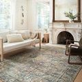 Margot rug displayed in cozy room with light wood sofa and blanket accents by a fireplace