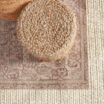 Top-down close-up of woven pouf resting on rug edge next to cream textured rug