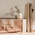 Lifestyle setting featuring rolled and flat earth-toned rugs contrasting with the grey Nador rug below vase