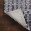 Corner of the Yeshaia Grey / Charcoal Rug flipped up, exposing beige woven backing