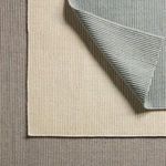 Stack of three ribbed rugs in cream, gray, and beige colorways with corner of top rug flipped over