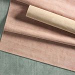 Rolled blush rug layered over a green rug highlighting color contrast and fabric luster