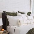 Murphy Pillow styled as large dark olive accent pillow behind white decorative pillows on bed with white brick wall