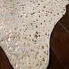 Close-up of Bryce rug edge showing gold metallic spots on a creamy beige pile over dark wood flooring