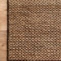 Corner view of Lily Natural Rug on wooden floor highlighting woven pattern and edge detail