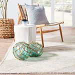 Close-up of rug under wooden bench styled with ceramic vase and dried palm leaves by window