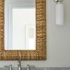 Sconce mounted next to a woven framed mirror showing metal arm and hardware details