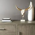 Partial console with decorative bull skull and tall white ceramic vase on top against neutral wall