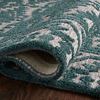 Rolled edge of teal and dove rug showing thickness and backing on dark wooden floor