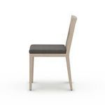Sherwood Brown outdoor dining chair beside wooden dining table on sunlit concrete patio with greenery background