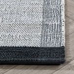 Rug corner detail displaying flat weave pattern and solid black end border on wood floor