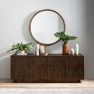 Dark wood sideboard below round wall mirror sitting partially on light area of Amaud rug