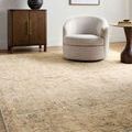 Rug shown in a room setting with beige club chair, wooden cabinet, and side table on light hardwood floor