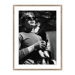 Black and white photograph of Andy Warhol wearing sunglasses and holding bananas, framed with a wooden border