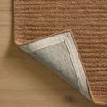 Rug corner flipped over revealing woven cotton backing and stitched edge on hardwood floor