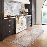 Runner rug placed in a kitchen setting with dark cabinetry and gold hardware on light hardwood floors