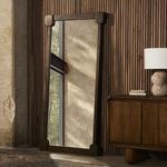 Harda Floor Mirror setup in room leaning against wood paneled wall with side cabinet and lamp