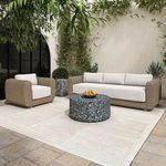 Outdoor side table styled as accent piece next to wicker armchair and sofa on tiled patio with greenery and light wall