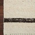 Top view close-up of rug's edge on wood floor highlighting woven texture and darker brown stripes