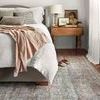 Close perspective of rug in bedroom focusing on texture contrast with soft bedding and natural light.