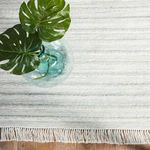 Top view of Torre rug under glass vase with monstera leaves showing linear textured pattern