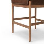 Close-up of warm-finished oak legs and footrest with brown leather seat underside