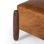 Close-up on ottoman corner with focus on leather texture and shape of rounded wooden leg