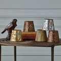 Multiple chandelier shades with varied hand-painted bird and leaf designs arranged on woven table in room