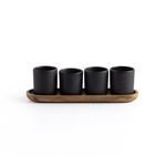 Overhead view of four matte black espresso cups arranged in a row on wooden tray against white background
