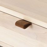Close-up showing brown leather drawer pull extending from light wood drawer front