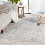 Seraph Medallion rug styled in living room with beige sofa, knit throw, wooden side table, and window background