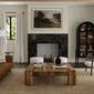 Living room interior with painting hung above dark stone fireplace flanked by windows and neutral furniture