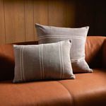 Two pillows, square and rectangular, placed on a leather sofa in warm wood-paneled room