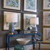 Pair of lamps on blue lacquered console table below framed botanical artwork in a gray room