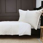 Cream-colored Monaco Coverlet on bed with quilted pattern, 1-inch flange, and matching pillows in a dark brown room