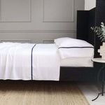Langston Bamboo Sateen Sheet Set in white with navy trim on a queen bed in a modern bedroom