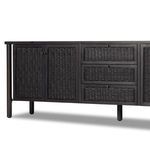 Angled front view emphasizing the contrast between woven cane drawer fronts and black wash wood frame.