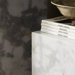 Close-up showing top of marble pedestal with stacked books and ceramic bowl in ambient room light