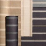 Assortment of rolled and flat indoor/outdoor rugs with similar striped patterns in navy, beige, and light blue shades
