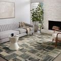 Rug displayed in a bright room with gray sofa, white walls, large windows, and fireplace